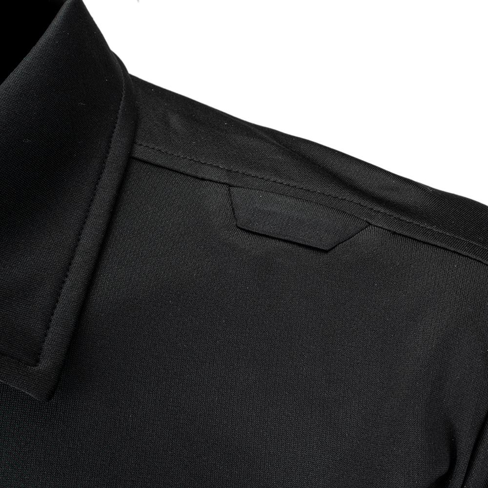 Close-up detail shot of a black polo shirt showcasing the shoulder seam, a small hidden pocket, and the textured fabric