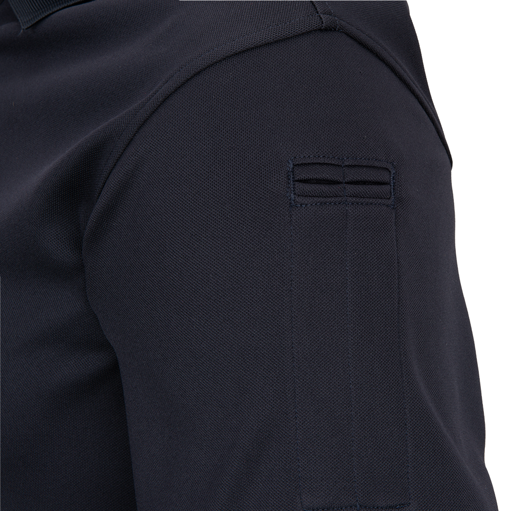 Close-up detail of a dark navy pique polo shirt showing a unique three-stitched pocket on the sleeve with subtle ribbed texture and a hint of collar