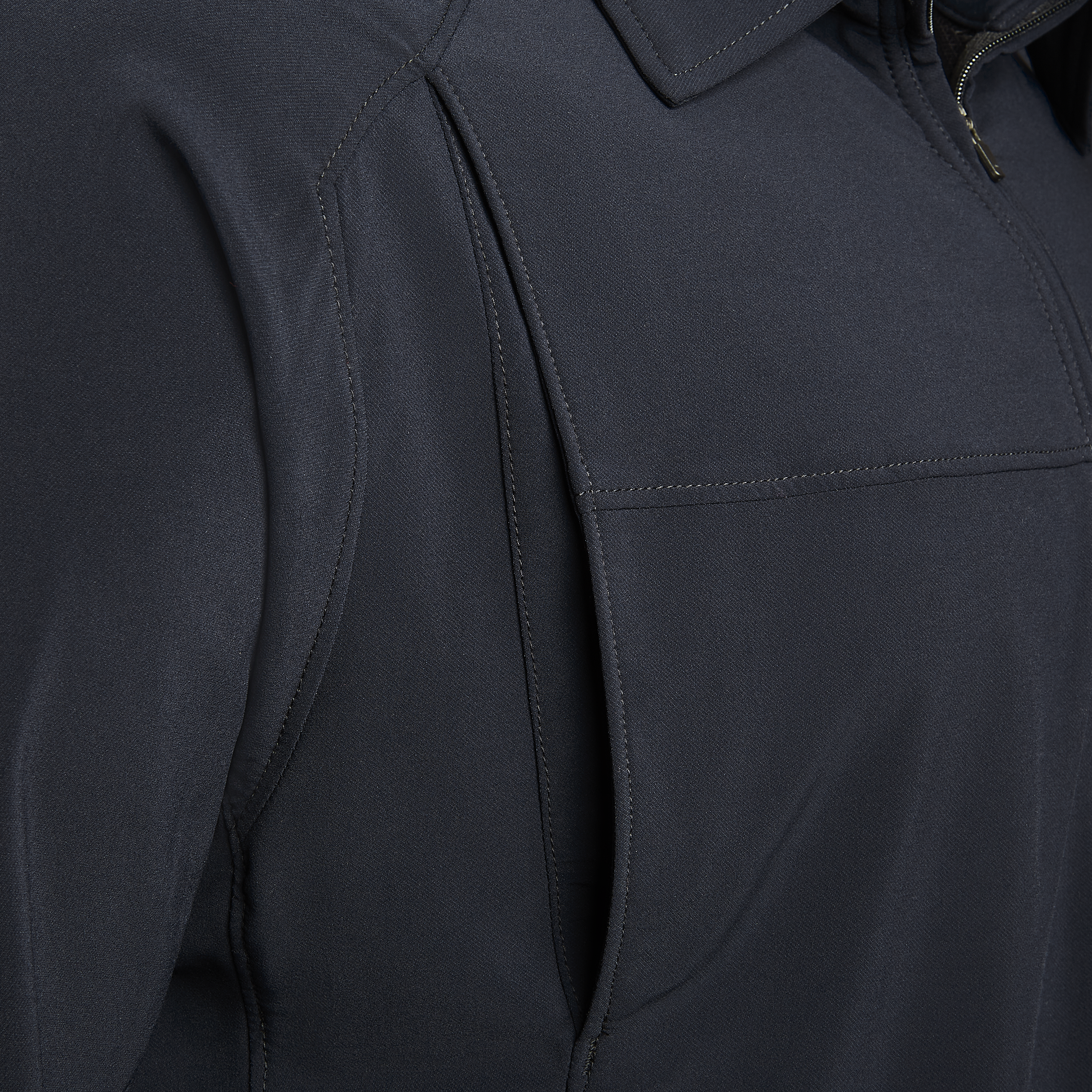 Close-up detail shot of a dark navy softshell jacket showing subtle stitching, a zipper, and a unique pocket design