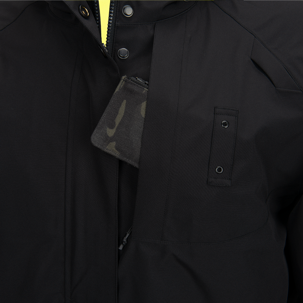 Product shot showing a black jacket with a camo-patterned interior pocket, visible black snaps, and a partially visible yellow zipper