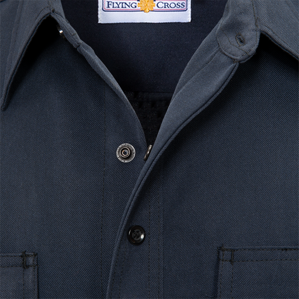 Close-up product shot of a dark gray Flying Cross brand work shirt showing the collar, buttons, and a woven label with subtle texturing and stitching details