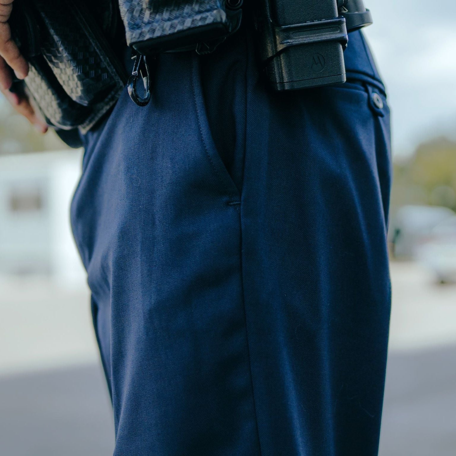 Photograph detail of a person wearing dark blue pants with a black gun holster and a textured black wallet featuring a small, dark zipper pull and subtle stitching detail