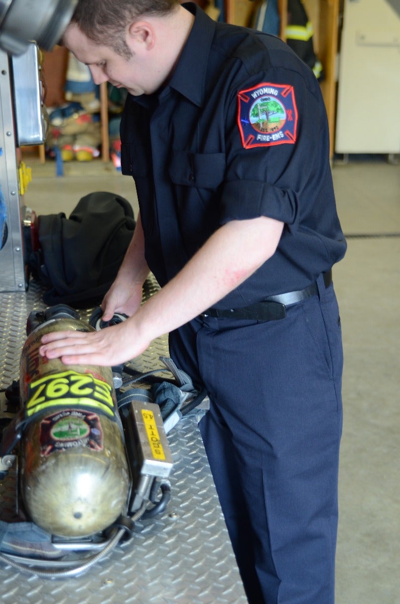 Photograph Wyoming Fire-EMS firefighter in fire station inspecting oxygen tank with number 262, a dark blue uniform with a patch and a diamond-plate surface.