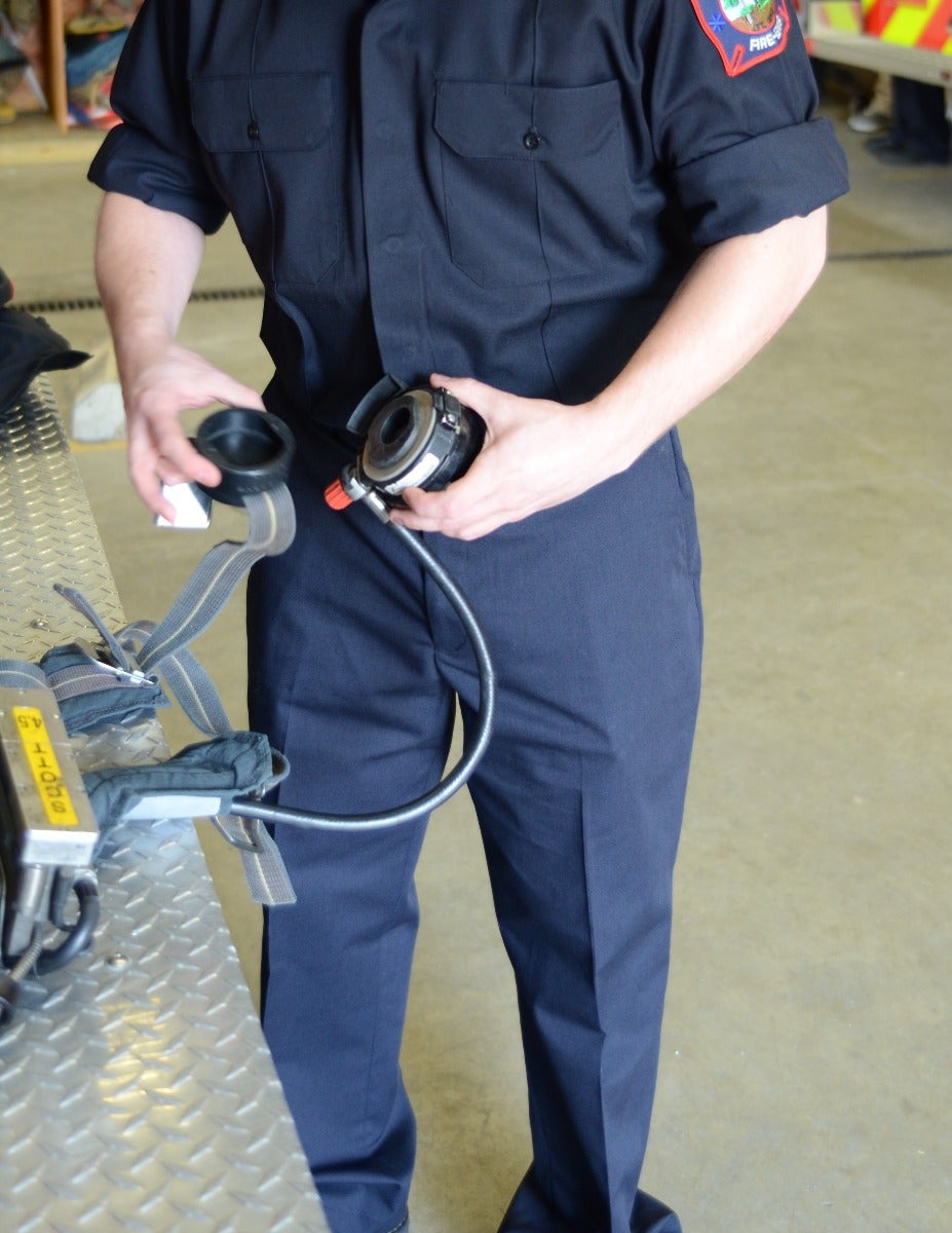 Photograph firefighter inspecting a self-contained breathing apparatus SCBA with a black hose and red valve in a fire station