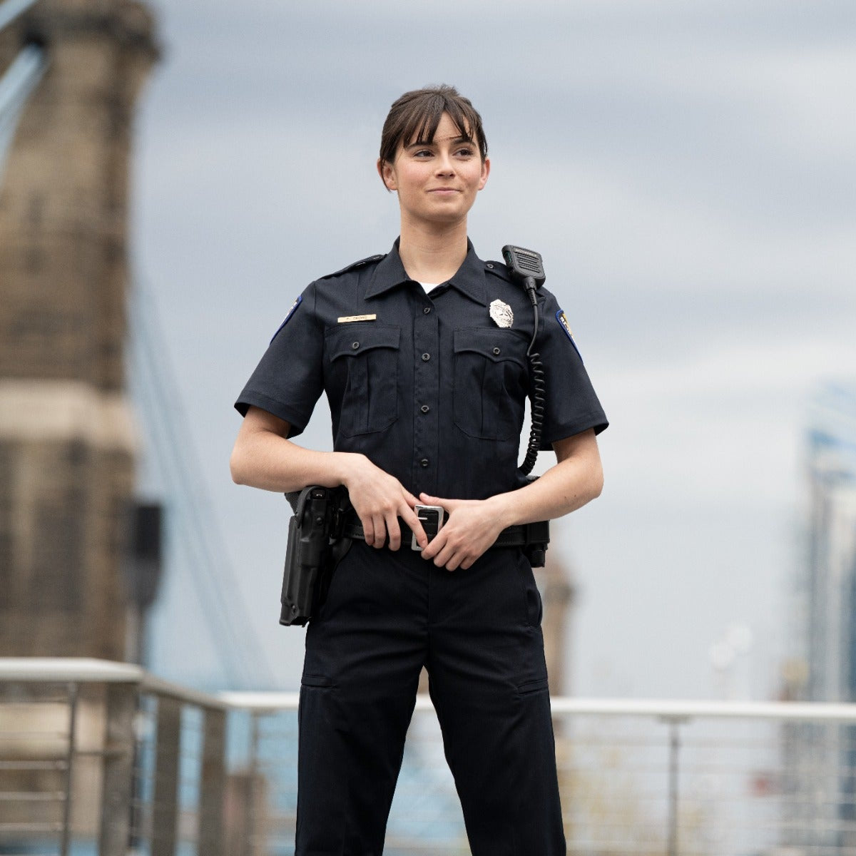 Photograph female police officer city bridge background dark uniform silver badge radio