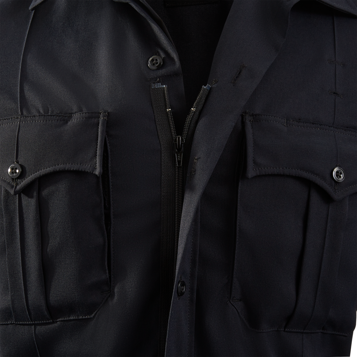 Close-up photograph of a dark navy blue uniform shirt showing a zipper, buttons, and flap pockets