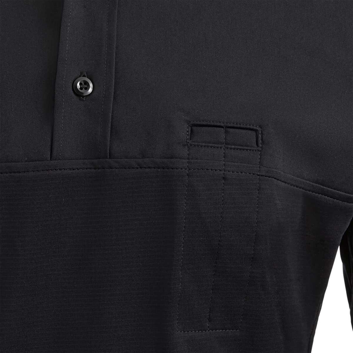 Close-up product shot of a dark-colored, textured polo shirt with a unique, subtly stitched pocket and a dark button detail showing fine craftsmanship