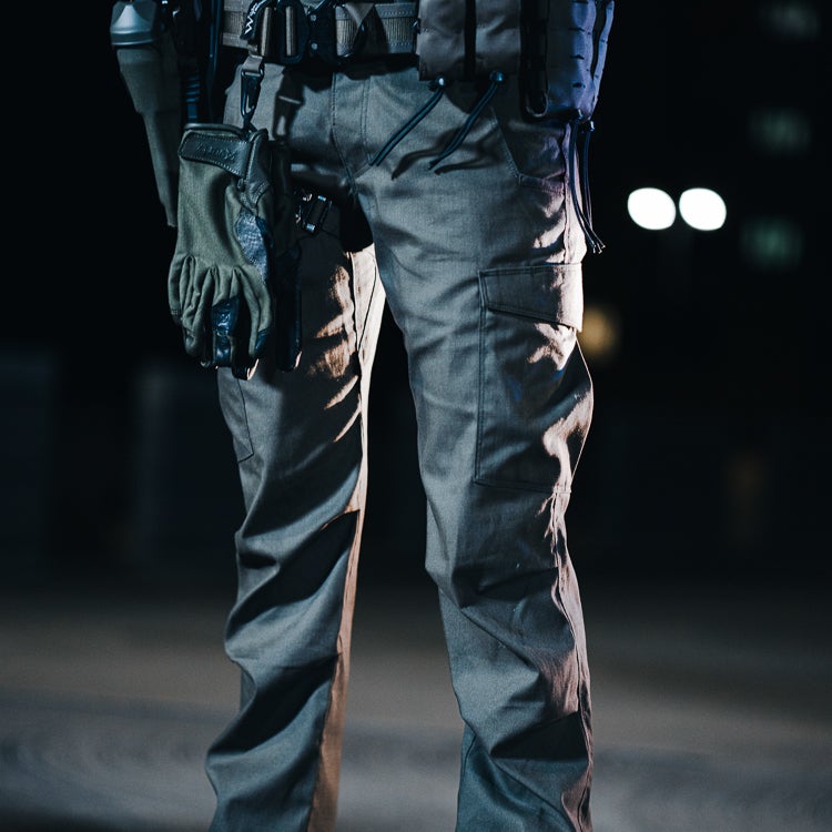 Photograph unknown artist a person wearing tactical pants and gloves at night with out of focus lights in the background showing cargo pockets and textured fabric