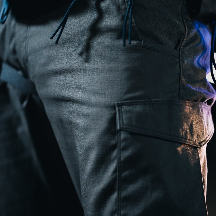 Here's a concise alt text description following all instructions:
Close-up photography of dark gray cargo pants showcasing detailed texture, flap pockets and drawstring waist