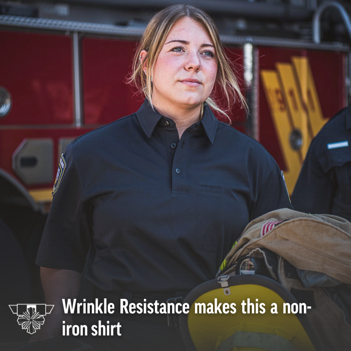 Photograph female firefighter in dark wrinkle-resistant polo shirt near firetruck with yellow stripes and red body holding folded fire hose and helmet showcasing embroidered badge and reflective details