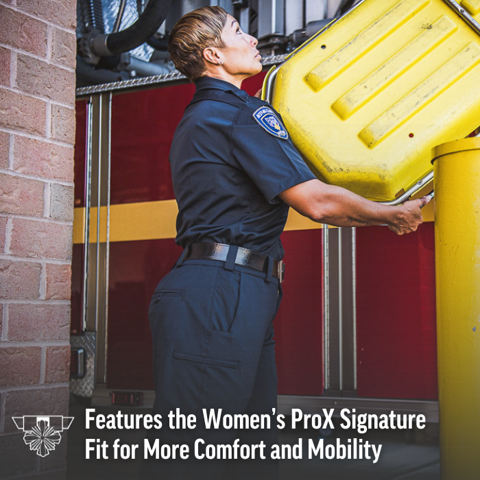 Photograph firefighter woman lifting yellow equipment near red firetruck with yellow stripes and brick building showcasing a dark-navy uniform and black belt
