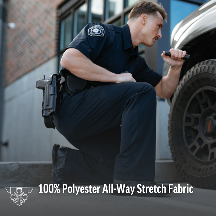Photography of a police officer in black uniform inspecting a vehicle near a brick building with a flashlight and a firearm in a black holster showcasing dark pants with all-way stretch fabric and a city patch