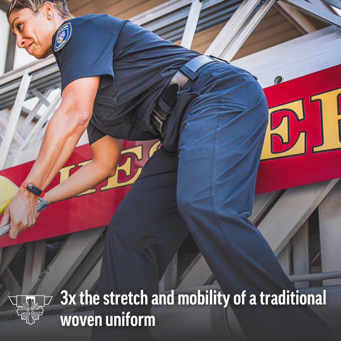 Photograph of a firefighter in dark blue uniform pants and shirt near a firetruck with red and yellow lettering and metallic ladder details a yellow safety device and a smartwatch are visible