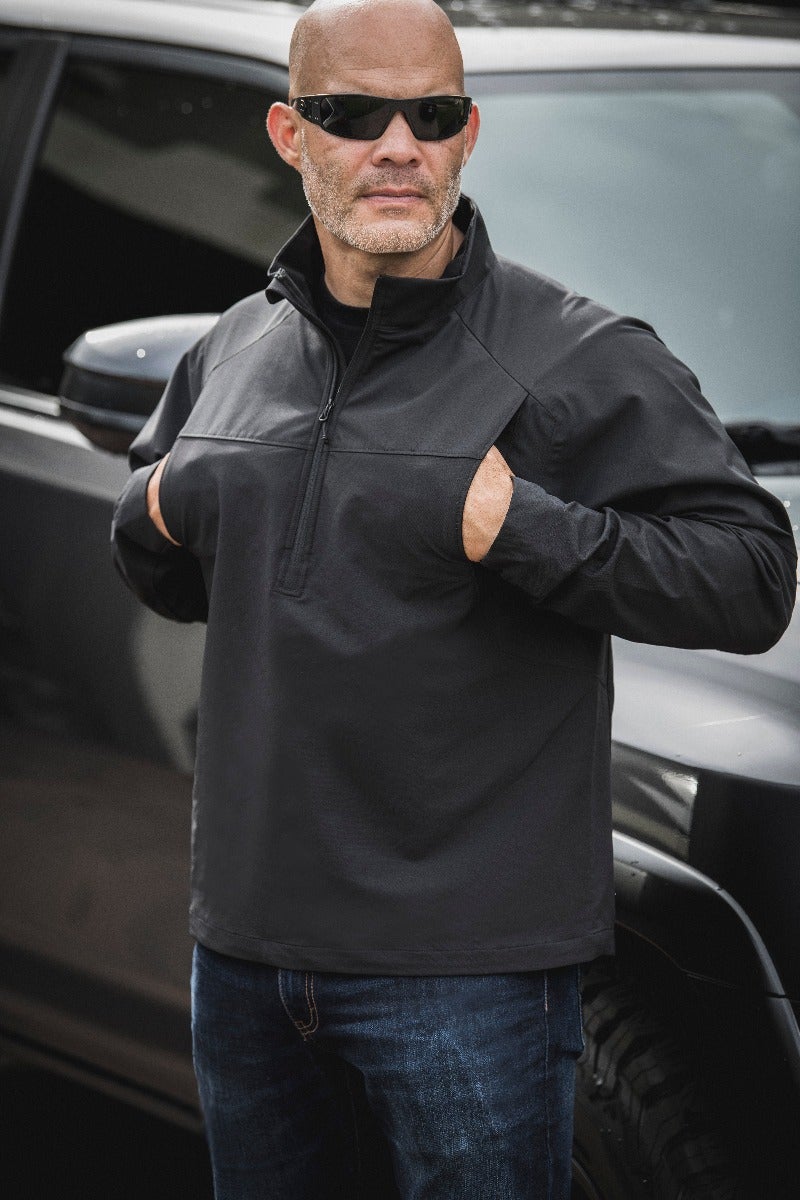 Photograph of a man wearing a black zip-up shirt with unique sleeve pockets standing near a dark-colored SUV showcasing a casual yet stylish look with dark sunglasses and blue jeans