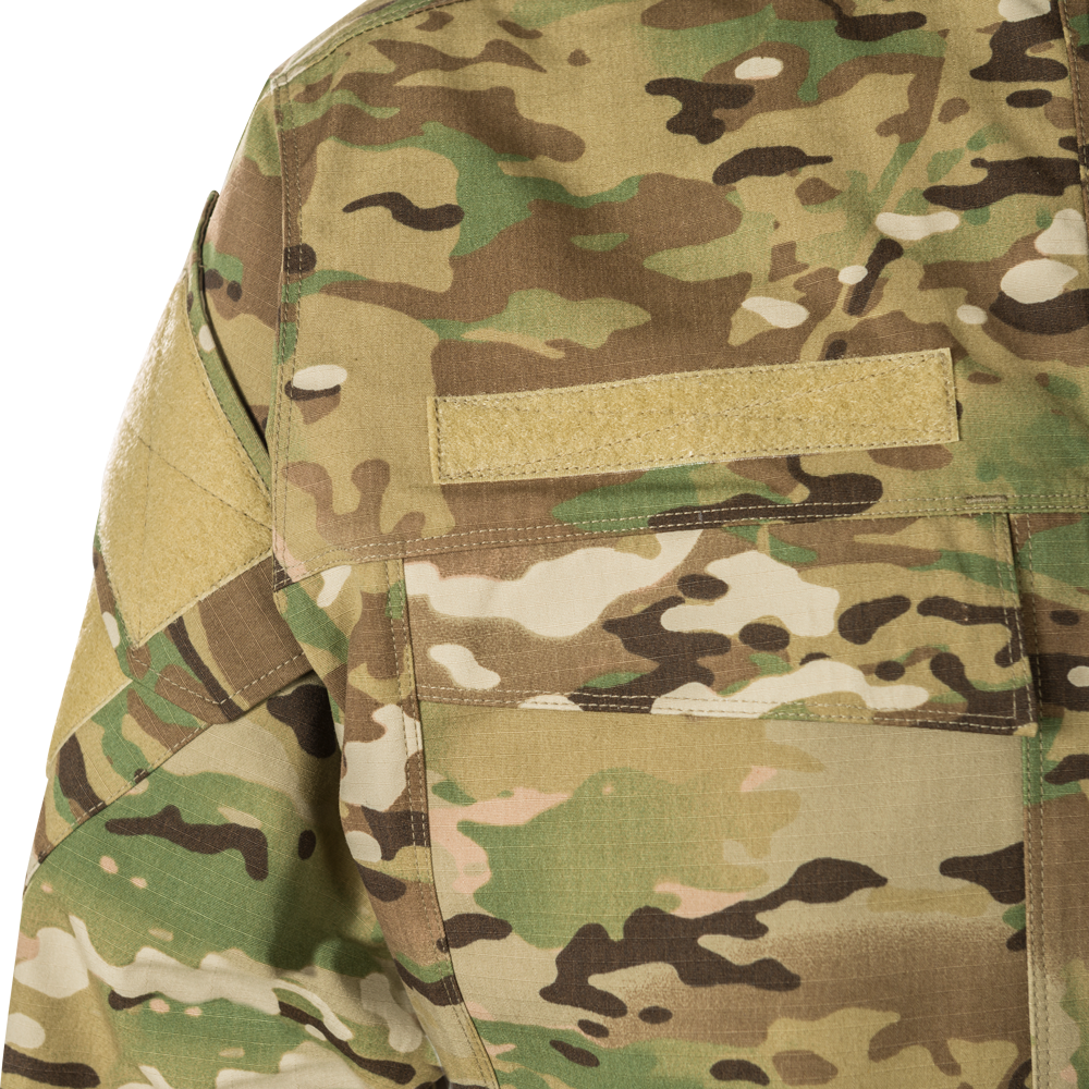 Close-up of OCP camouflage fabric showing tan shoulder patch, stitching detail, and muted green, brown, and beige tones
