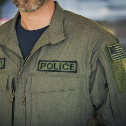 Close-up photograph of a police uniform featuring a POLICE patch, an American flag patch, and olive-green fabric with textured details
