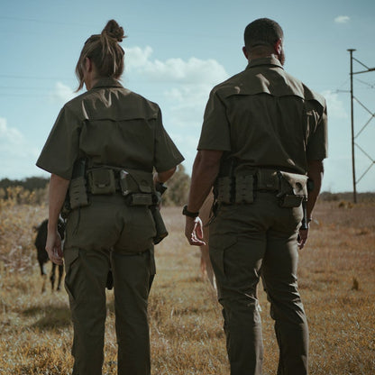 Unidentified artist photograph two uniformed officers walking in a field near power lines with a dark animal and tan, olive green uniforms and utility belts