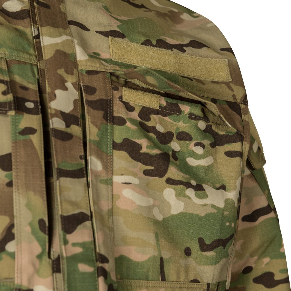 Close-up photograph of a camouflage fabric military uniform showing tan and green patterns, featuring velcro patches and multiple pockets