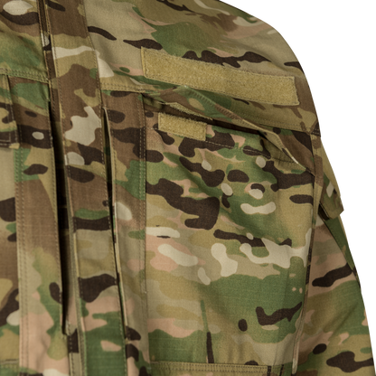 Close-up photograph of a camouflage fabric military uniform showing tan and green patterns, featuring velcro patches and multiple pockets