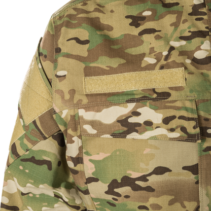 Close-up of OCP camouflage fabric showing tan shoulder patch, stitching detail, and muted green, brown, and beige tones
