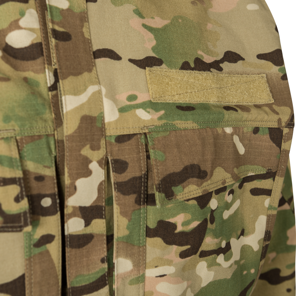 Close-up photograph of OCP camouflage fabric showing a tan nametape and chest pockets with subtle stitching details and a multi-toned pattern of greens, browns, and tans.
